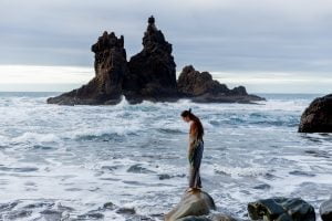 Person, die allein auf den Felsen vor dem Meer steht.