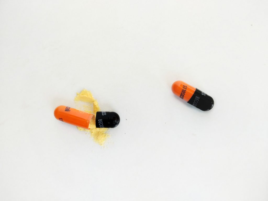Zwei Pillen auf weißem Hintergrund, eine ist offen, wobei Puder ausläuft.