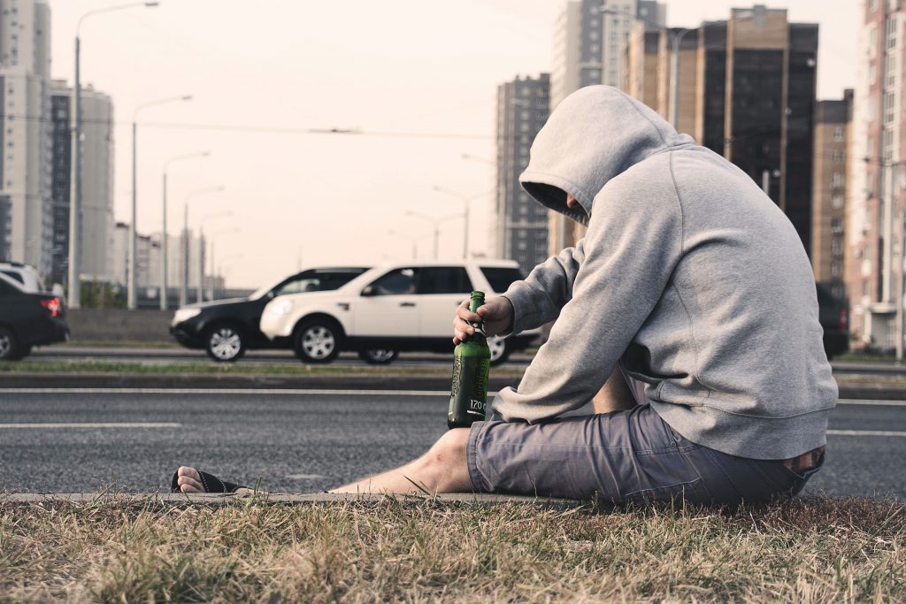 Mann sitzt auf der Seitenstraße mit einer Flasche Alkohol in der Hand.