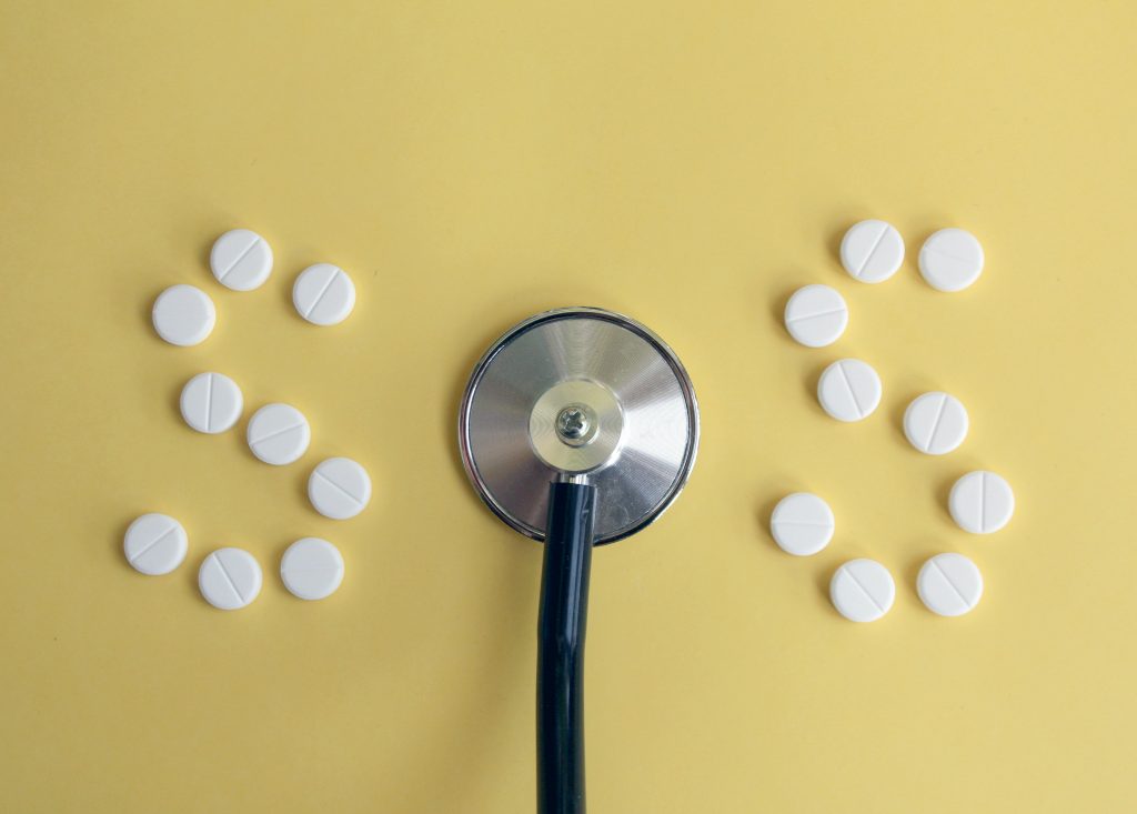 Weiße Pillen, die in einer 'S'-Form mit einem Stethoskop in der Mitte angeordnet sind, um SOS zu buchstabieren.